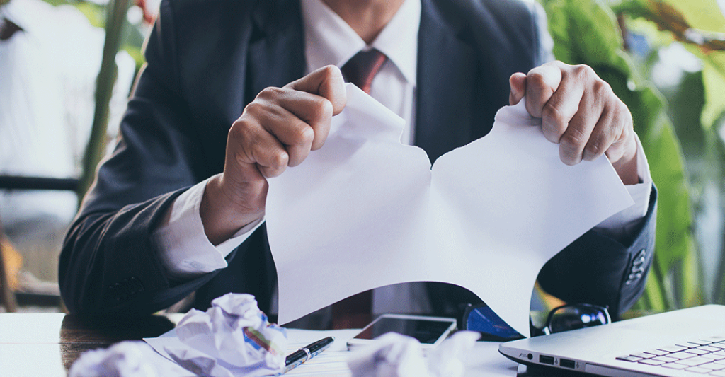 Persona rompiendo un contrato, sobre una mesa de oficina profesional.
