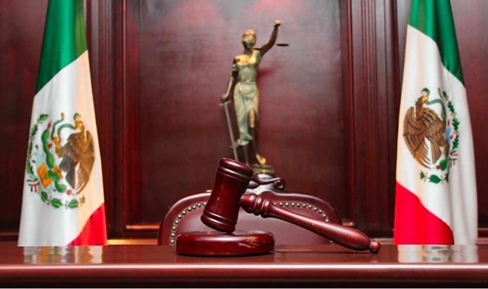 Mazo judicial sobre un escritorio frente a dos banderas de México.
